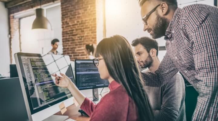 A mortgage processor enters data at her desk while a supervisor looks over her shoulder.