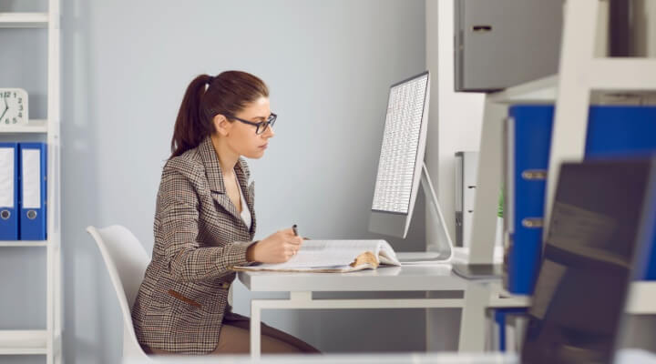 Female accountant works behind desk doing ledgers and bookkeeping in a business process outsourcing center.