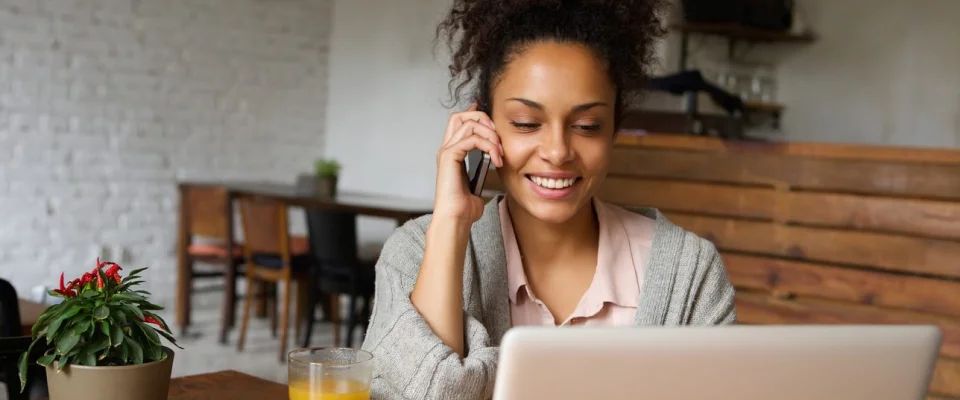 African American woman calling by phone and using a laptop in a cafeteria.