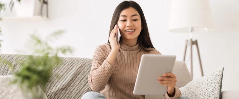 Young woman sitting on a couch while making a call and using a tablet.